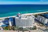 High-rise multi-story building featuring tiered balconies, a rooftop deck, and direct proximity to the oceanfront