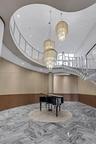 Grand foyer featuring a sweeping curved staircase with polished metal railings, tiered crystal chandeliers, stone flooring in a herringbone pattern, a