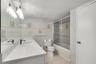Bathroom featuring a quartz-topped vanity with an integrated basin, ceramic tile flooring, full-width wall mirror, and a tub-shower combination enclos