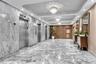 Polished stone flooring in a herringbone pattern, full-height stone wall cladding, stainless steel elevator doors, recessed tray ceiling with multi-ti