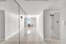 Interior hallway featuring light-toned tile flooring, floor-to-ceiling mirrored wall panels, and recessed lighting