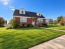 Brick exterior featuring dual front-facing dormers, a shingled roof, a covered entryway, and manicured landscaping