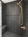 Shower stall featuring matte black subway wall tile, herringbone-patterned floor and niche tile, integrated stone-finish bench, and brass-finish fixtu