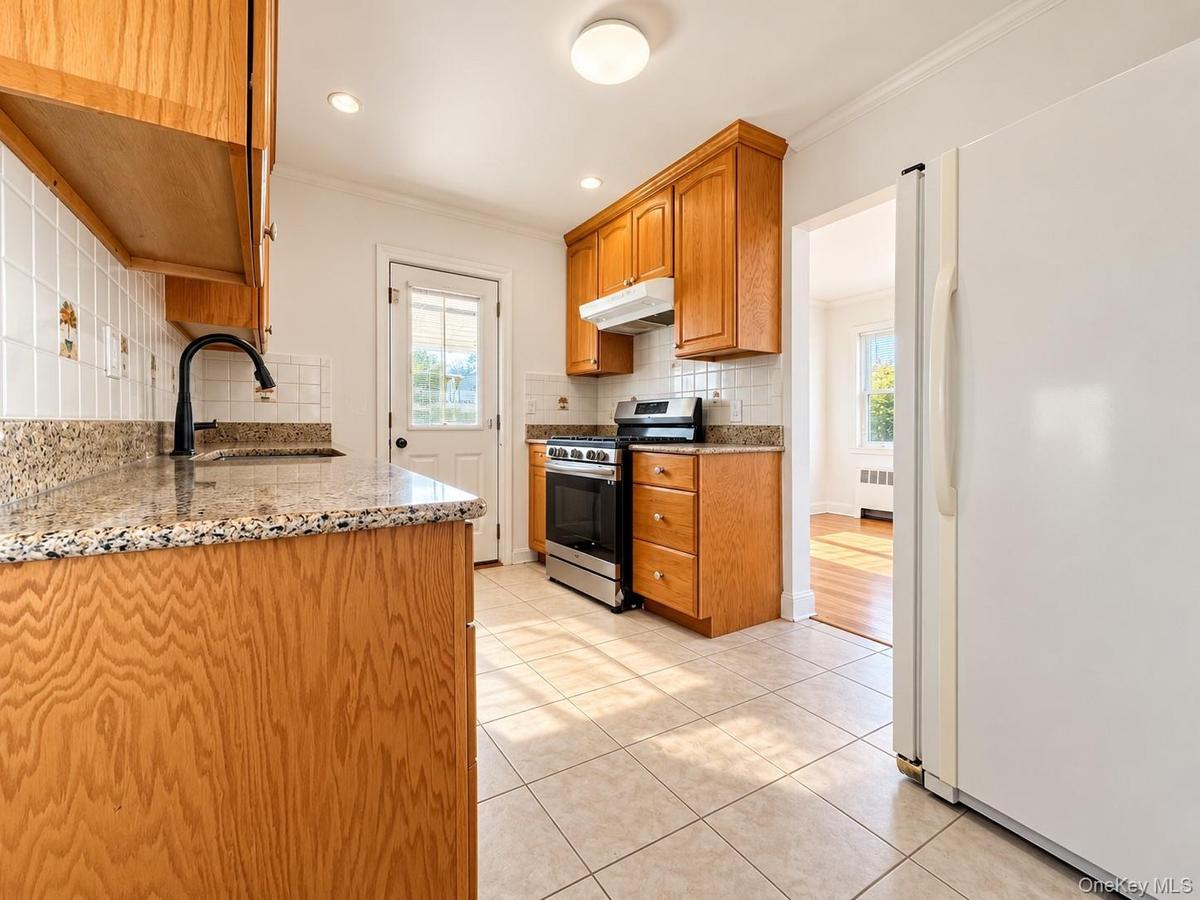 Kitchen featuring wood cabinetry, stone-finish countertops, tile backsplash, stainless steel range, and tile flooring