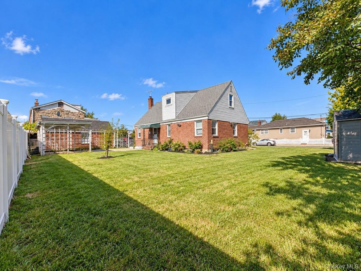 Spacious backyard featuring a manicured lawn, a detached wooden pergola, white vinyl fencing, and a detached storage shed