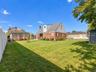 Spacious backyard featuring a manicured lawn, a detached wooden pergola, white vinyl fencing, and a detached storage shed