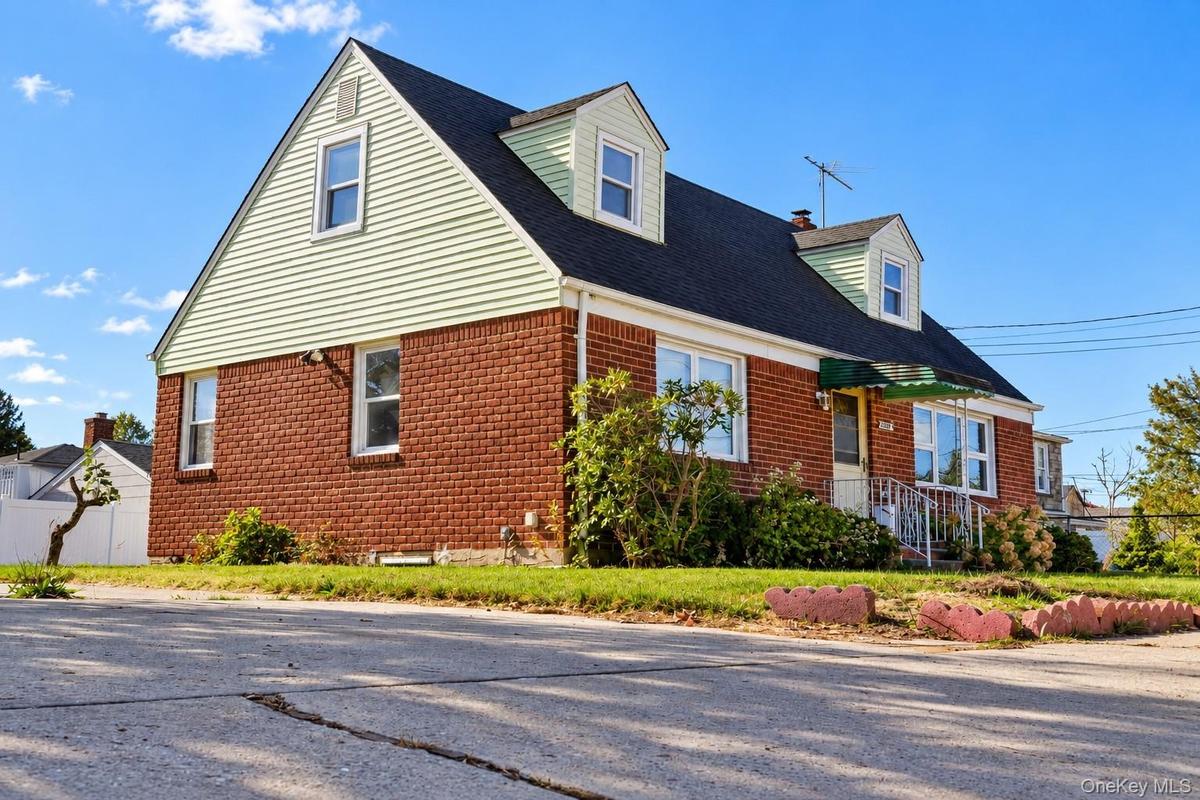 Cape Cod style exterior featuring brick masonry, light-toned horizontal siding, two roof dormers, and a paved driveway