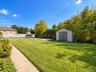 Expansive backyard featuring a level lawn, concrete walkway, detached storage shed, and mature perimeter landscaping