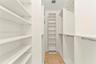 Walk-in closet featuring white custom built-in shelving, adjustable storage units, metal garment rods, and stone-tile flooring