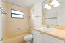 Bathroom featuring a neutral-toned tile shower surround, a built-in tub, a white vanity with a light-colored countertop, and a large-format mirror wit