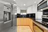 Kitchen featuring stainless steel appliances, dark stone countertops, high-gloss upper cabinetry, wood-finish lower cabinetry, and tile flooring