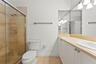 Walk-in shower with stone tile surround, vanity with stone countertop, integrated undermount sink, expansive vanity mirror, and polished metal fixture