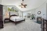 Vaulted ceiling with a central multi-blade ceiling fan, expansive trapezoidal window, fireplace with a tiled hearth and mantel, and wall-to-wall carpe