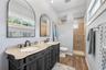 Dual-sink vanity with stone countertop and dark cabinetry, arch-top mirrors, wood-finish flooring, and a tiled shower enclosure