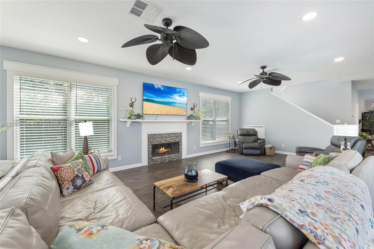 Living area featuring dark wood-finish flooring, recessed lighting, ceiling fans, and a fireplace with a textured stone surround and mantle