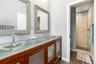 Double vanity featuring a translucent glass countertop with integrated dual basins, wooden cabinetry with frosted glass panels, two framed mirrors, an