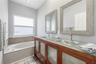 Dual-sink vanity with a translucent glass countertop and wood cabinetry, paired with a built-in soaking tub featuring mosaic tile surround and dual wa