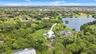 Aerial perspective featuring a multi-story residence situated on a landscaped lot with mature trees and proximity to a lake
