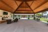 Expansive covered patio featuring a vaulted wood-plank ceiling, exposed timber trusses, concrete flooring, and a built-in linear electric fireplace