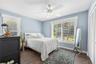 Room with wood-finish flooring, white ceiling fan with integrated light fixture, dual windows with blinds, and white louvered closet doors