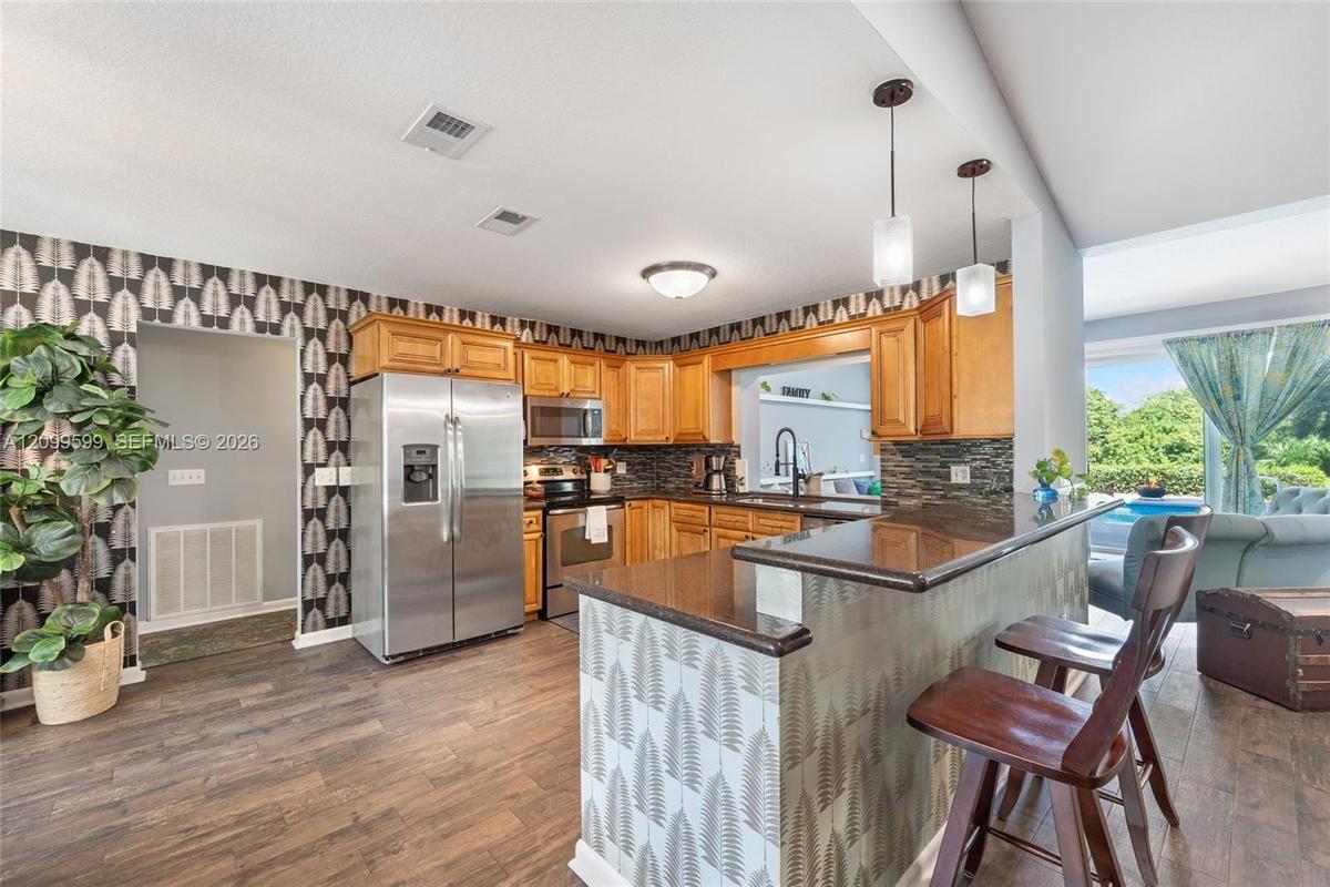 Kitchen featuring wood cabinetry, stainless steel appliances, stacked stone backsplash, and a breakfast bar with stone-finish countertop and pendant l