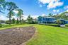 Expansive rear grounds featuring a circular stone fire pit, manicured lawn, perimeter landscaping, and mature trees