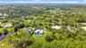 Aerial perspective featuring a multi-story residence with a metal roof, an in-ground swimming pool, a stone-paved patio, and established mature trees 