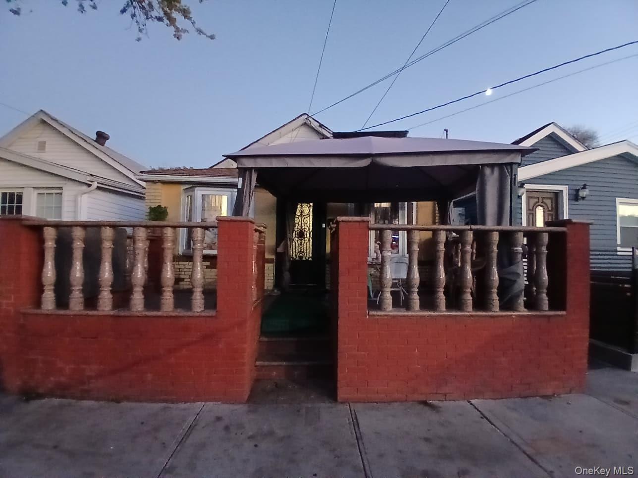 Front patio featuring red masonry walls, stone-finish balustrades, and a decorative metal entry door