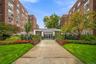 Brick masonry exterior featuring a central glass-paneled entryway, concrete walkway, and landscaped garden beds with mature trees