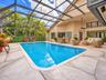 Screened-in outdoor living area featuring a custom-shaped swimming pool with built-in stairs, decorative concrete patio decking, and a ceiling fan