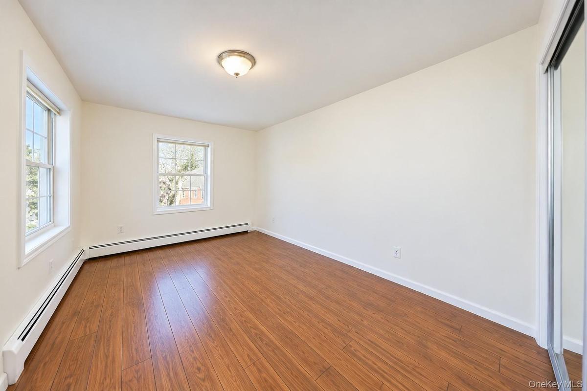 Room featuring wood-finish flooring, dual windows, a flush-mount ceiling light fixture, and mirrored sliding closet doors