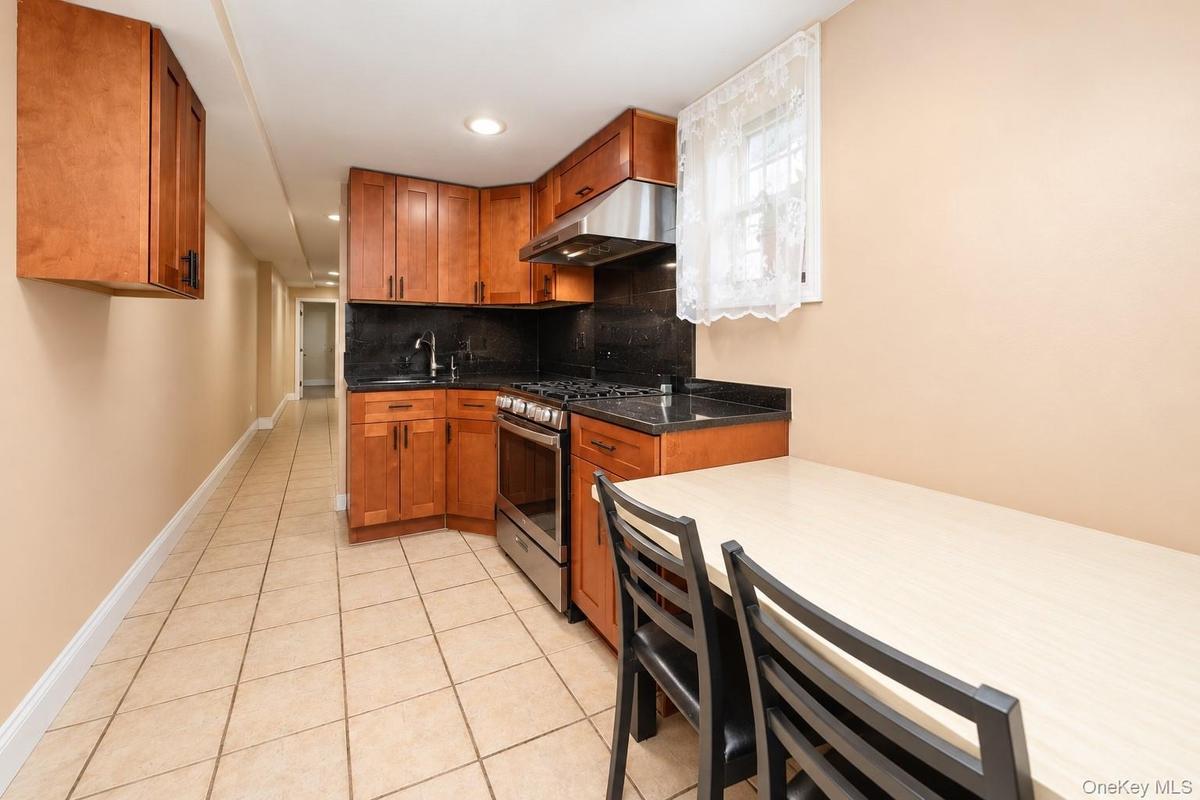 Kitchen featuring wood cabinetry, stone countertops, stainless steel gas range, stainless steel range hood, and tile flooring