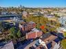Aerial perspective of a multi-story masonry building with a flat roofline situated in an established urban setting featuring mature tree cover