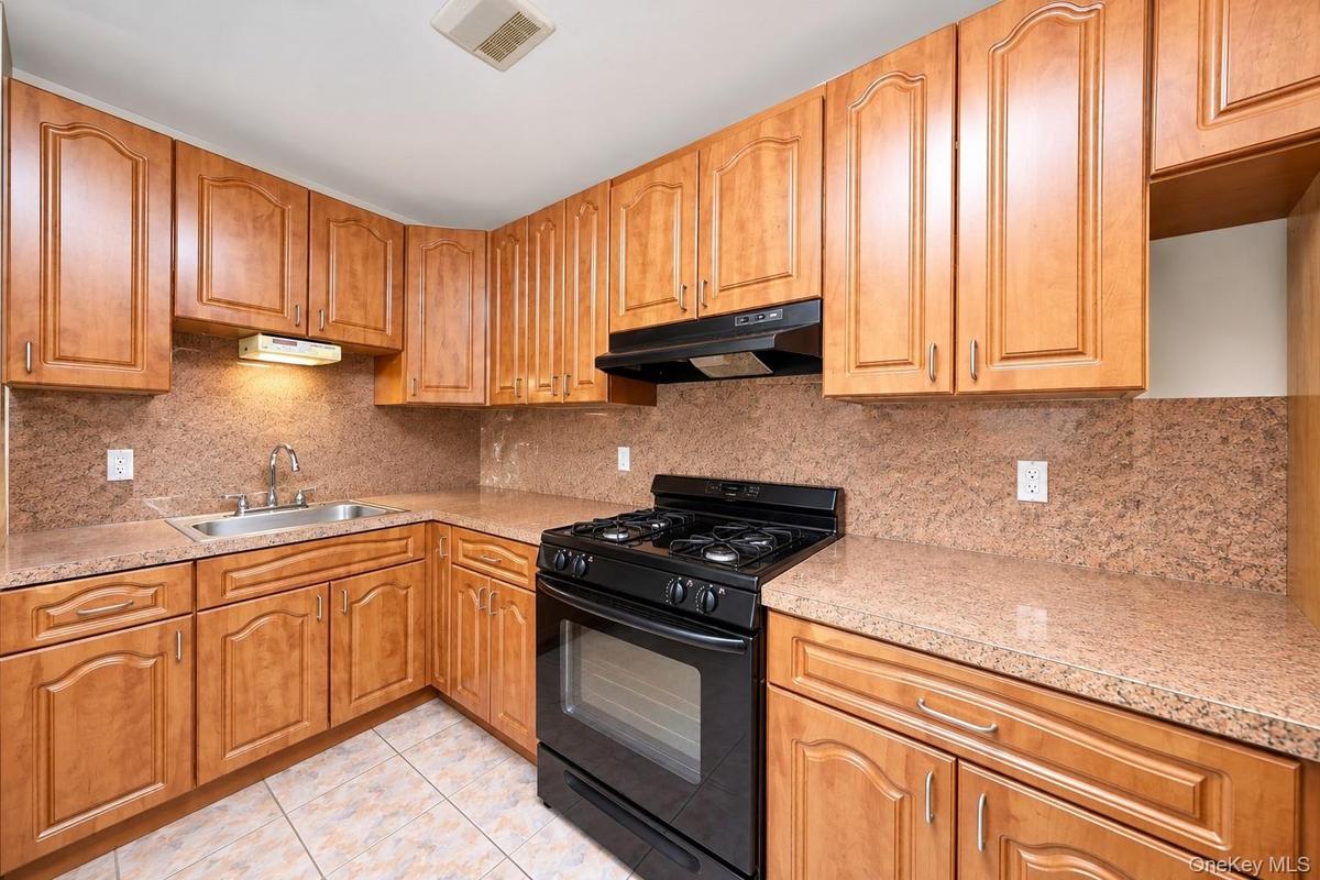 Kitchen featuring wood cabinetry, stone-surface countertops, full-height stone backsplash, under-cabinet lighting, and integrated black gas range