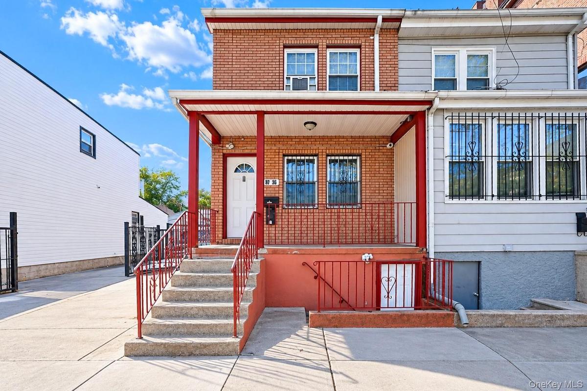 Brick facade exterior featuring a covered front porch, concrete steps, metal railings, and dual-pane windows with security bars