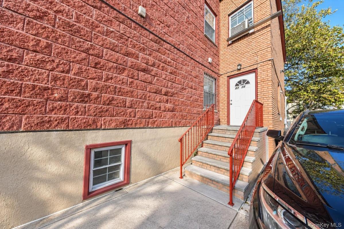 Exterior featuring red textured masonry, tan stucco lower siding, concrete staircase with metal railings, and white entry door with arched transom win