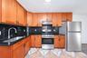 Kitchen featuring natural-finish wood cabinetry, black countertops, stainless steel appliances, and a geometric-pattern tile floor