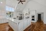 Kitchen featuring vaulted ceilings, wide-plank wood-finish flooring, white shaker-style cabinetry, a quartz surface peninsula, and stainless steel bui