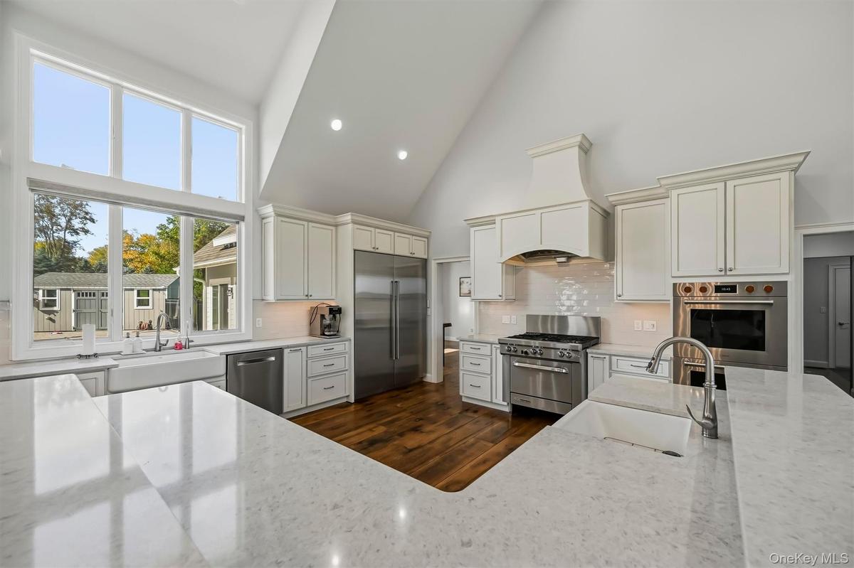 Kitchen featuring high vaulted ceilings, expansive windows, custom white cabinetry, quartz surface countertops, and wood-finish flooring