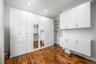 Custom floor-to-ceiling white cabinetry with integrated drawer storage, mirrored paneling, open shelving, and wood-finish flooring