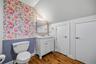 Bathroom featuring wood-finish flooring, floral accent wallpaper, wainscoting, a vanity with a light-toned stone countertop, and a built-in medicine c