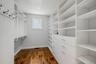 Custom storage organization featuring white floor-to-ceiling shelving, built-in dresser drawers with metallic hardware, integrated garment rods, wall-