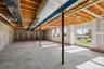 Unfinished space featuring exposed timber joist ceiling, concrete flooring, concrete foundation walls, structural support columns, and sliding glass e