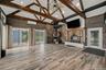 Vaulted ceilings with exposed timber trusses, wood-finish flooring, stone-accentedwood burning fireplace with a timber mantel, integrated stone-clad p