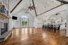 Vaulted ceilings with exposed timber beams, floor-to-ceiling stone fireplace, wide-plank wood-finish flooring, and natural light via arched glass door