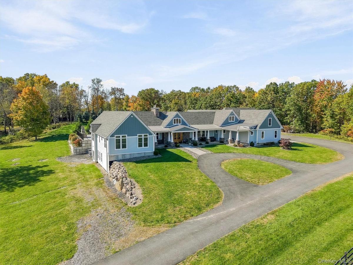 Expansive residence featuring a multi-gabled roofline, lap siding exterior, a wrap-around covered porch with stone-base columns, a circular driveway, 