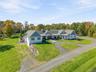 Expansive residence featuring a multi-gabled roofline, lap siding exterior, a wrap-around covered porch with stone-base columns, a circular driveway, 