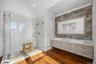 Dual vanity with white vessel sinks and stone countertop, walk-in glass-enclosed shower featuring white subway tile, and wood-finish flooring