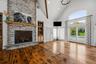 Vaulted ceilings with exposed beams, floor-to-ceiling stone  gas fireplace with wood mantel, wood-finish flooring, built-in shelving, and oversized gl