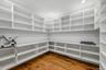 Walk-in pantry featuring floor-to-ceiling white built-in shelving, expansive solid surface countertops, and wide-plank wood-finish flooring